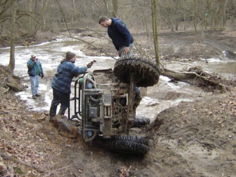 1992 Ford Bronco - An ATV has overturned in a muddy ditch, with several people attempting to assist.