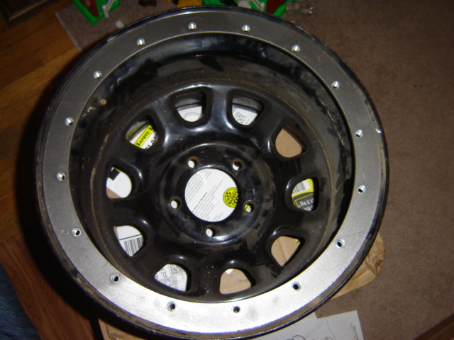Black aftermarket wheel with a metal ring bolted around the rim