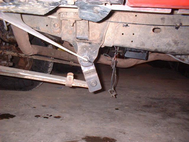 Truck undercarriage with leaf springs and exhaust pipe visible. Red paint on upper body