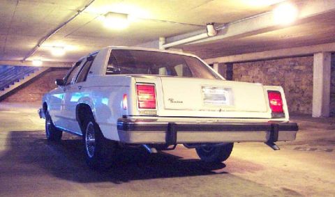 1985 Ford Crown Victoria LTD - Rear view of a white 1985 Ford Crown Victoria LTD parked in a dimly lit parking garage.