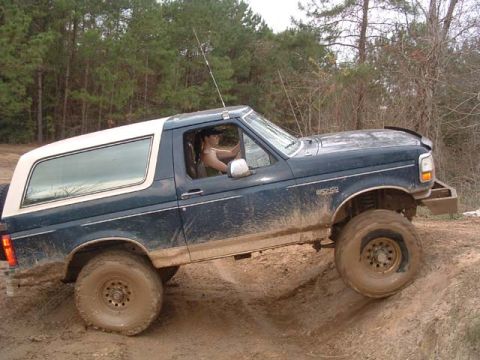 1993 Ford Bronco - A blue Ford Bronco navigates a muddy off-road trail.