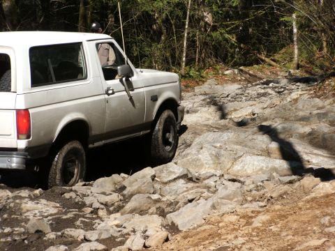 1980 Ford Bronco - White Ford Bronco tackling a challenging rocky terrain on an off-road trail.
