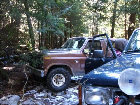 1980 Ford Bronco - Two off-road vehicles are parked on a rocky trail in a wooded area.