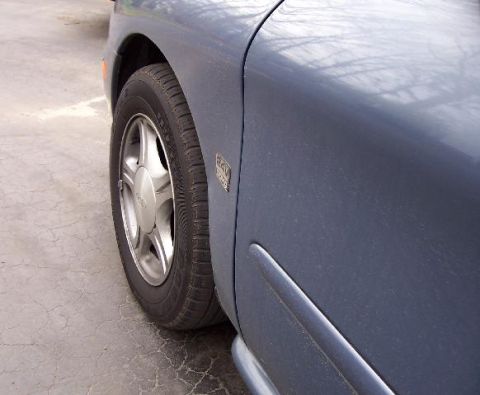 1999 Ford Taurus - Side view of a blue sedan, revealing the front wheel and fender detail.