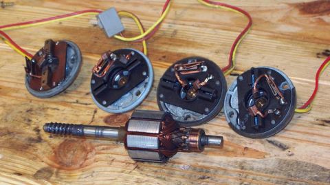 1985 Ford Crown Victoria LTD - Disassembled window motors and armature components are laid out on a wooden workbench.