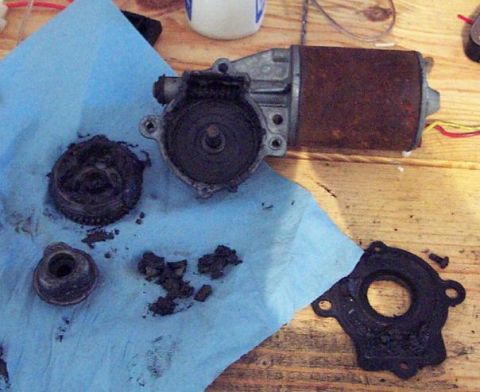 1985 Ford Crown Victoria LTD - Disassembled window motor components, including a rusty cylinder and gears, are laid out on a blue paper towel.