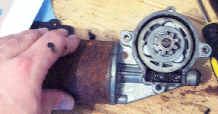 Rusty window motor with exposed gears and a hand holding it