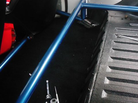 1978 Ford Bronco - The interior of a vehicle features a blue roll cage and black carpeting, with tools scattered on the floor.
