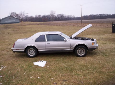 1992 Lincoln Mark VII - A silver coupe with its hood open sits in a field next to a building.