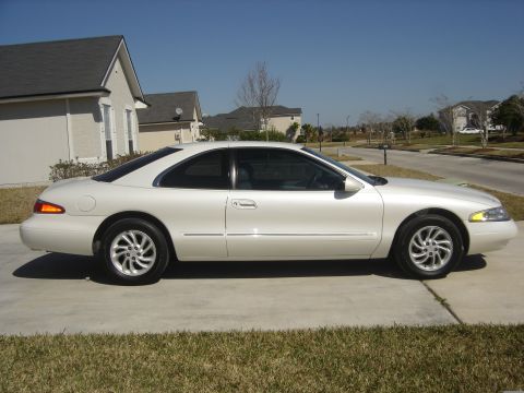 1997 Lincoln Mark VIII - A white 1997 Lincoln Mark VIII coupe is shown from the side, parked in front of a suburban house.