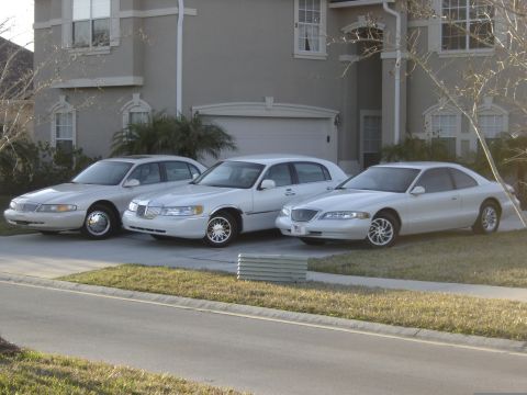 1997 Lincoln Mark VIII - Three white Lincoln vehicles are parked in front of a house. The vehicle on the right appears to be a Lincoln Mark VIII.