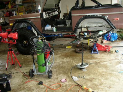 1995 Ford Bronco - Ford Bronco in garage with fender removed, showing suspension and parts laid out for repair.