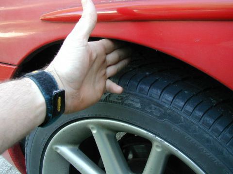 1994 Ford Probe - A hand is shown checking the clearance between a red car's fender and the tire.