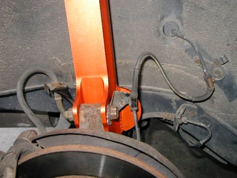 1994 Ford Probe - Close-up view of an aftermarket orange strut tower brace installed on a vehicle's suspension, showing brake lines and rotor.
