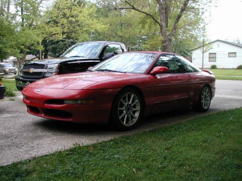 1994 Ford Probe - A red 1994 Ford Probe is parked in a driveway next to a black Chevrolet Silverado truck.