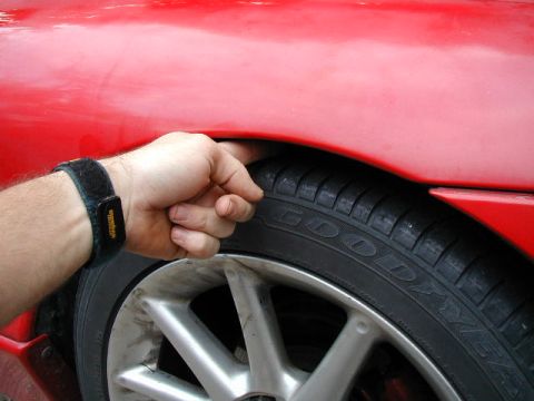 1994 Ford Probe - A hand is shown checking the clearance between a red car's fender and the tire.