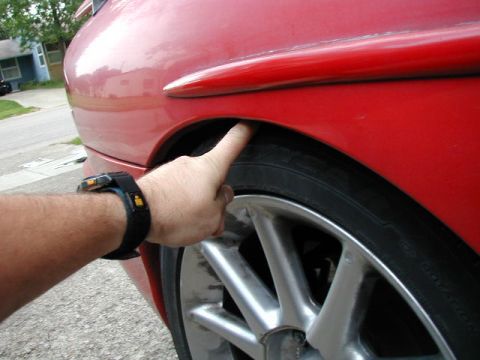 1994 Ford Probe - A finger points to the clearance between a red car's fender and tire, indicating a potential modification.