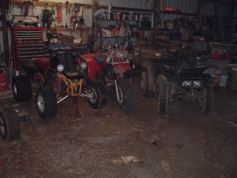 1995 Mercury Grand Marquis - A collection of ATVs are stored in a workshop, with tools and shelves visible in the background.