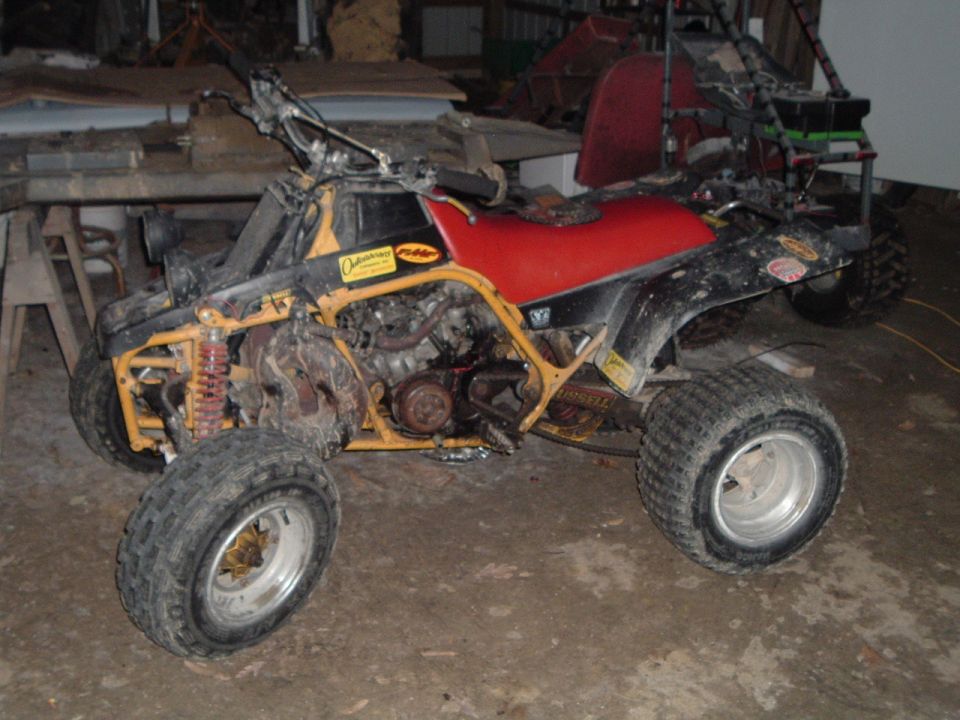 Muddy yellow-framed sport quad ATV with red seat parked in a dim garage