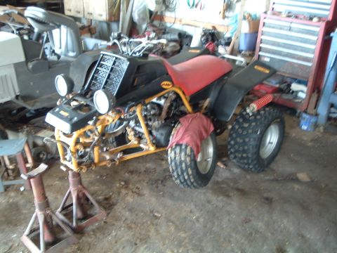 1995 Mercury Grand Marquis - An ATV with a red seat and black bodywork is supported by jack stands in a cluttered garage setting.