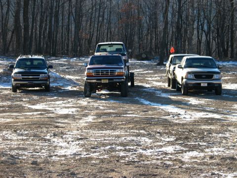 1995 Ford Bronco - Four trucks are parked in a lot with snow on the ground and trees in the background.