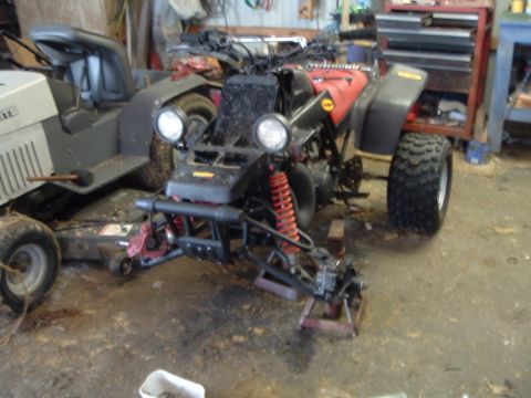 1995 Mercury Grand Marquis - A red ATV is parked in a garage, supported by jack stands, with a riding mower nearby.