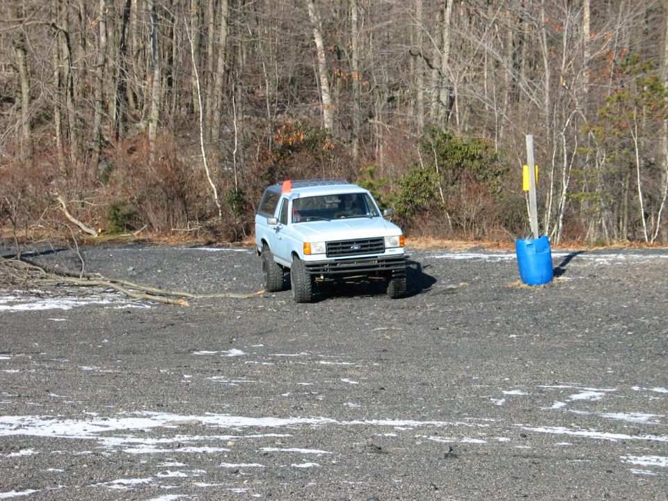 Light blue SUV with a camper shell, front bumper modified, parked on gravel lot