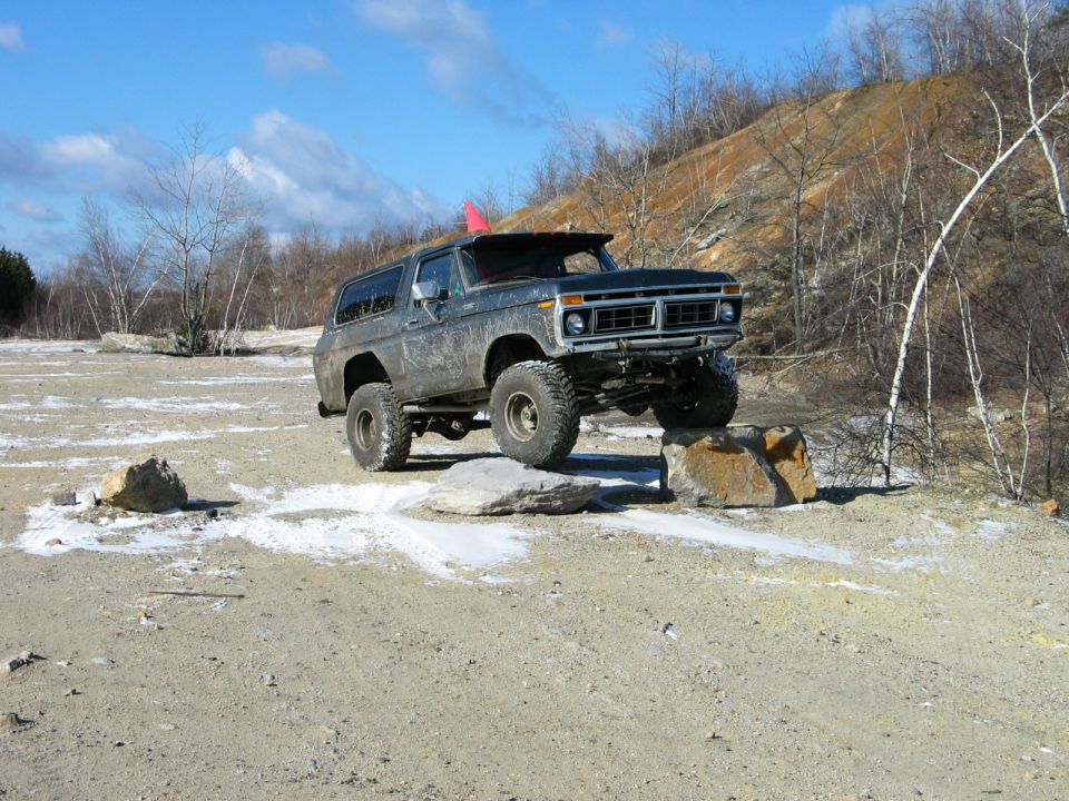 Modified Ford Bronco with large tires driving over rocks on a dirt trail
