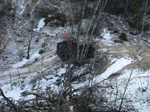 1995 Ford Bronco - A dark SUV is partially obscured by trees and appears stuck on a snowy, muddy slope.
