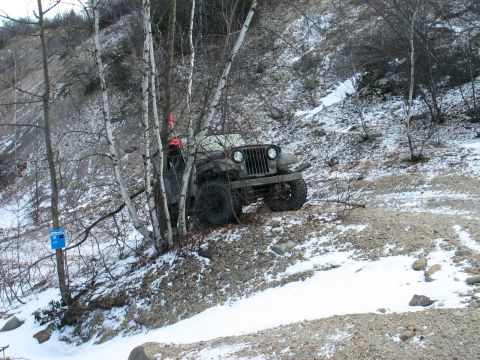1995 Ford Bronco - An olive green jeep is parked on a snowy, rocky hillside, partially obscured by trees.