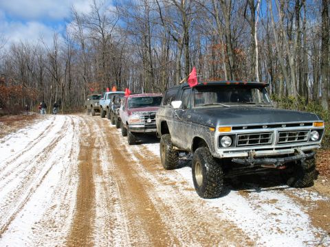 1995 Ford Bronco - A line of off-road vehicles, including a 1976 Ford Bronco, travel down a snowy dirt road through a wooded area.