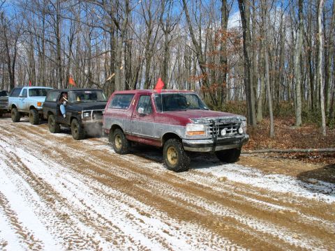 1995 Ford Bronco - Several off-road vehicles, including a 1995 Ford Bronco, are parked on a trail with snow and mud.