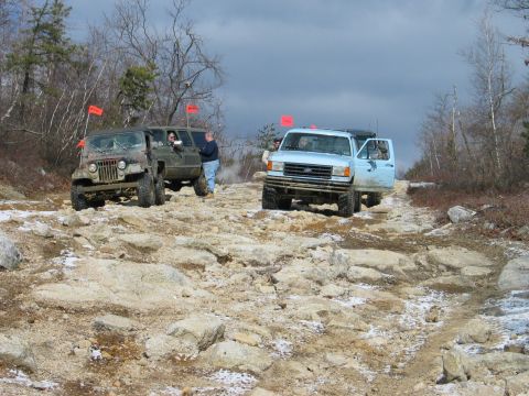 1995 Ford Bronco - Two off-road vehicles navigate a challenging, rocky path under a cloudy sky.