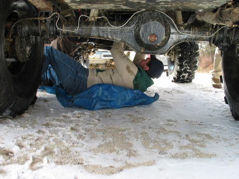 1995 Ford Bronco - A person works on the undercarriage of a vehicle in a snowy, outdoor environment.