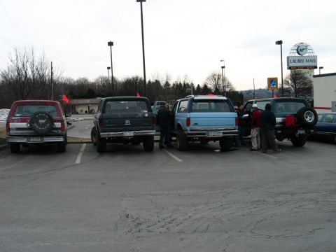 1995 Ford Bronco - Four Ford Broncos are parked in a lot, with a group of people gathered near two of them.