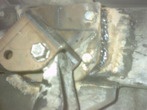 1992 Ford Bronco - Close-up flash photo of a fabricated steel mounting plate welded to a chassis bracket, with a heavy hex bolt through it and a thick bead of…