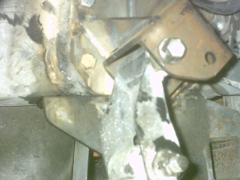1992 Ford Bronco - Blurry flash close-up under a vehicle showing a welded steel mounting bracket with a hex nut and stud, attached to a rusty frame member. We…