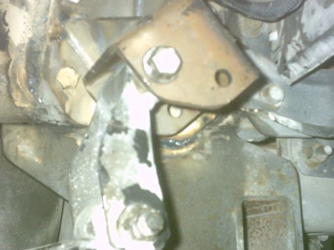 1992 Ford Bronco - Flash-lit underside shot of a steel bracket with a large hex nut and stud passing through it, bolted to a grimy frame rail and crossmember.…