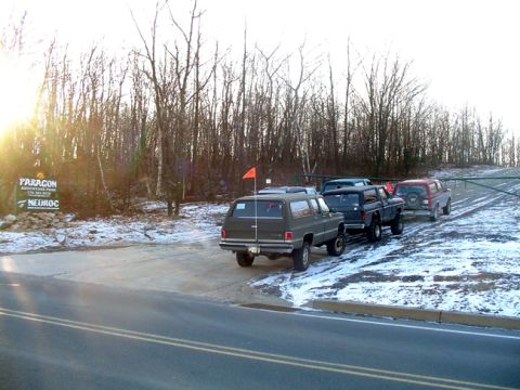 1979 Ford Bronco - A line of vehicles is parked on a snow-dusted road near a wooded area, with a sign for Paragon Adventure Park in the background.
