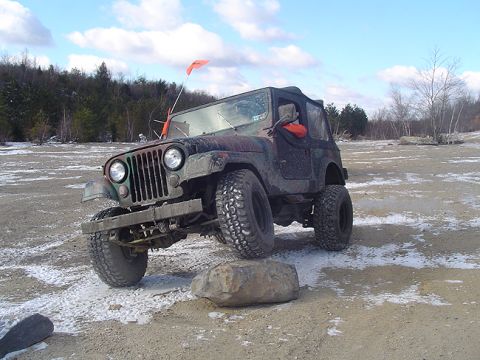 1979 Ford Bronco - A Jeep CJ-5 navigates an off-road course with a rock in its path.