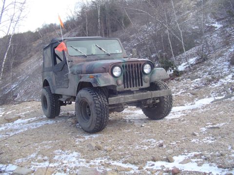 1979 Ford Bronco - A camouflaged Jeep CJ-5 navigates a snowy, wooded terrain.