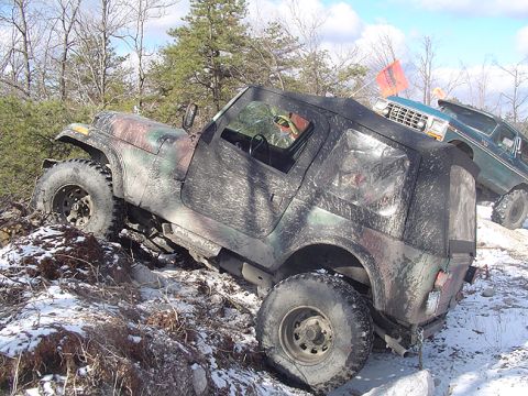 1979 Ford Bronco - A camouflaged Jeep Wrangler navigates a challenging snowy and rocky terrain, with another vehicle visible in the background.