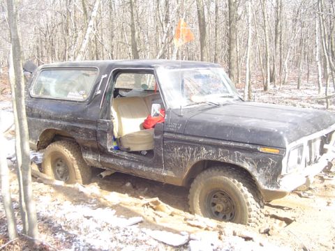 1979 Ford Bronco - A black 1978 Ford Bronco is stuck in the mud with its driver's door open, surrounded by trees.