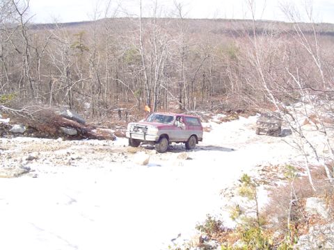 1979 Ford Bronco - A red and grey SUV navigates a snowy, wooded path with another vehicle visible in the background.