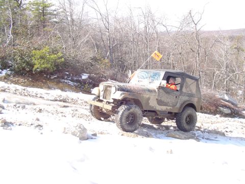 1979 Ford Bronco - A driver navigates a muddy Jeep over a snowy and rocky off-road path.