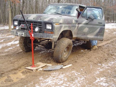 1979 Ford Bronco - A camouflage-painted Ford Bronco is stuck in the mud, with a hi-lift jack positioned to help free it.