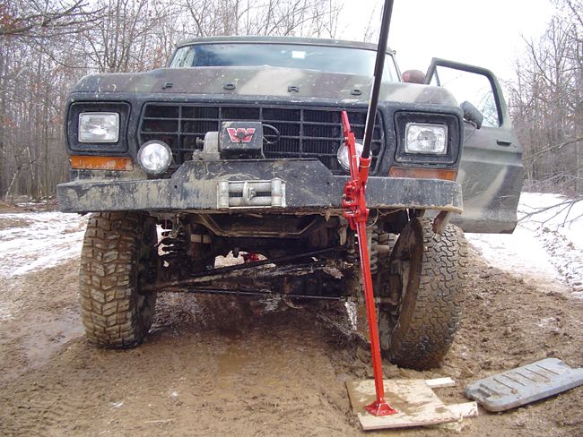 1979 Ford Bronco with camouflage paint, winch, and a red Hi-Lift jack stuck in mud