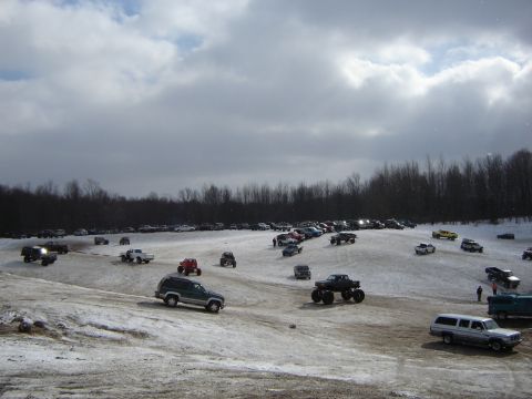 1978 Chevrolet C/K Pickup - A large gathering of trucks and SUVs are parked on a snowy field with trees in the background.