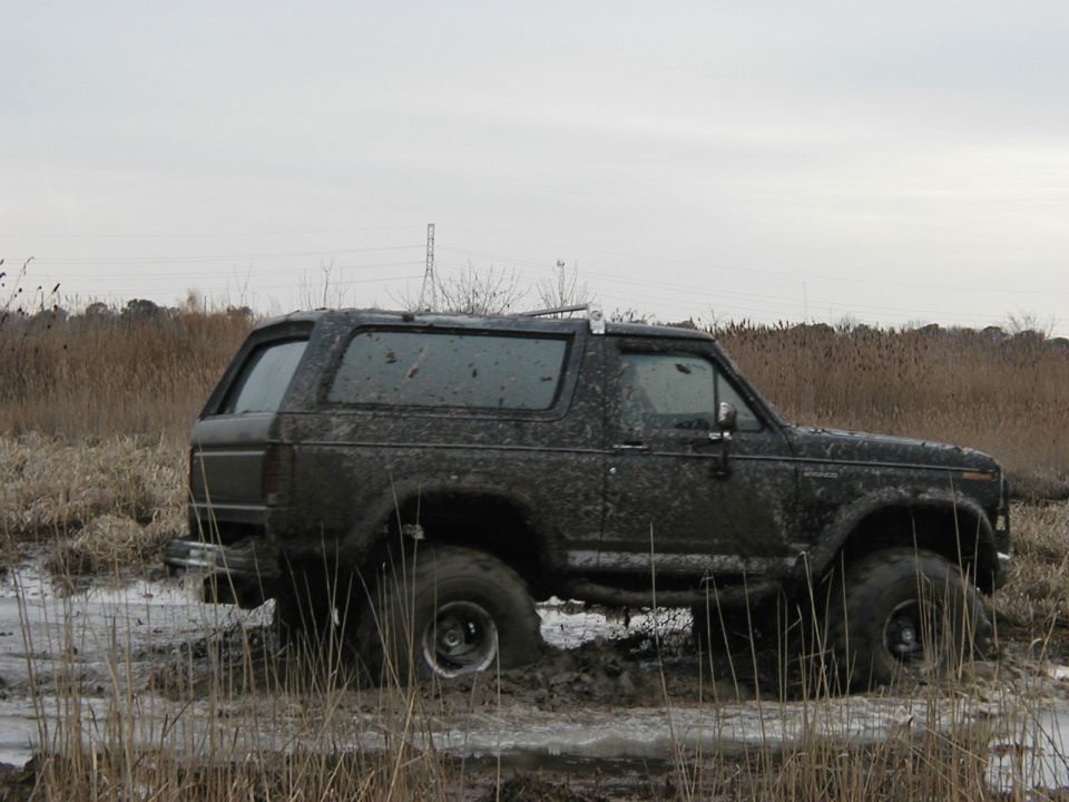 Mud-covered 1985 Ford Bronco stuck in a muddy field