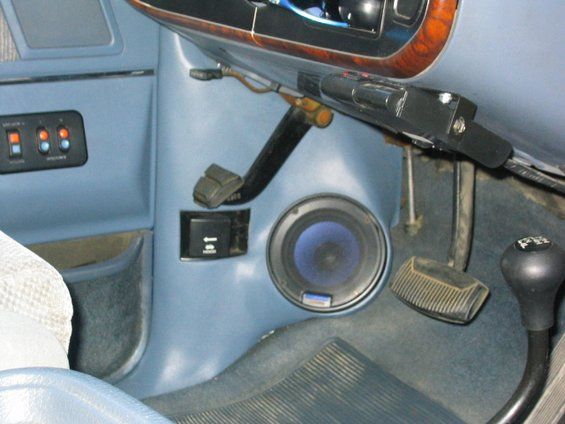 Blue vehicle interior with floor-mounted speaker, manual shifter, pedals and switches